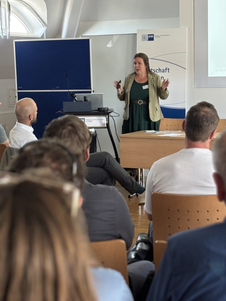 Referentin Sandra Schumann des KMI Leipzig hinter einem Redner:innen-Pult hält einen Vortrag vor dem Publikum der Veranstaltung "Leipzig vernetzt KI". 