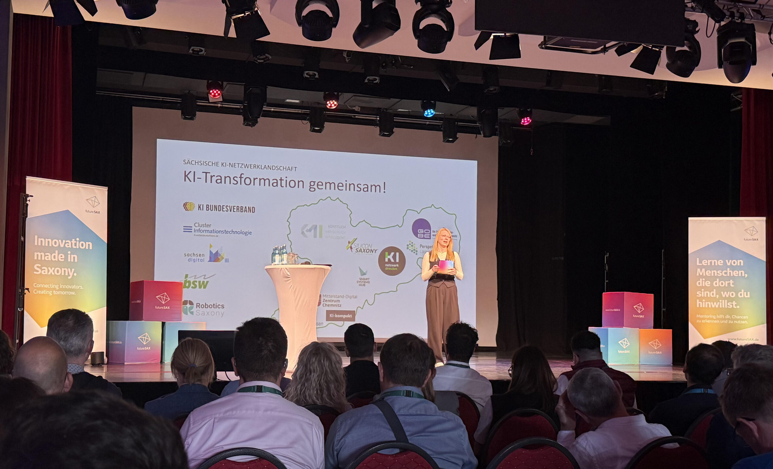 Das Publikum des futureSAX-Innovationsforums hört der Moderatorin auf der Bühne zu und schaut zu ihr.